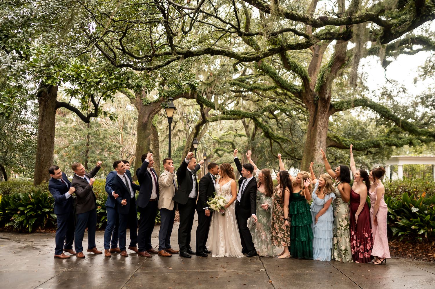 Wedding party poses beneath towering oak trees draped in Spanish moss at a Southern outdoor ceremony.