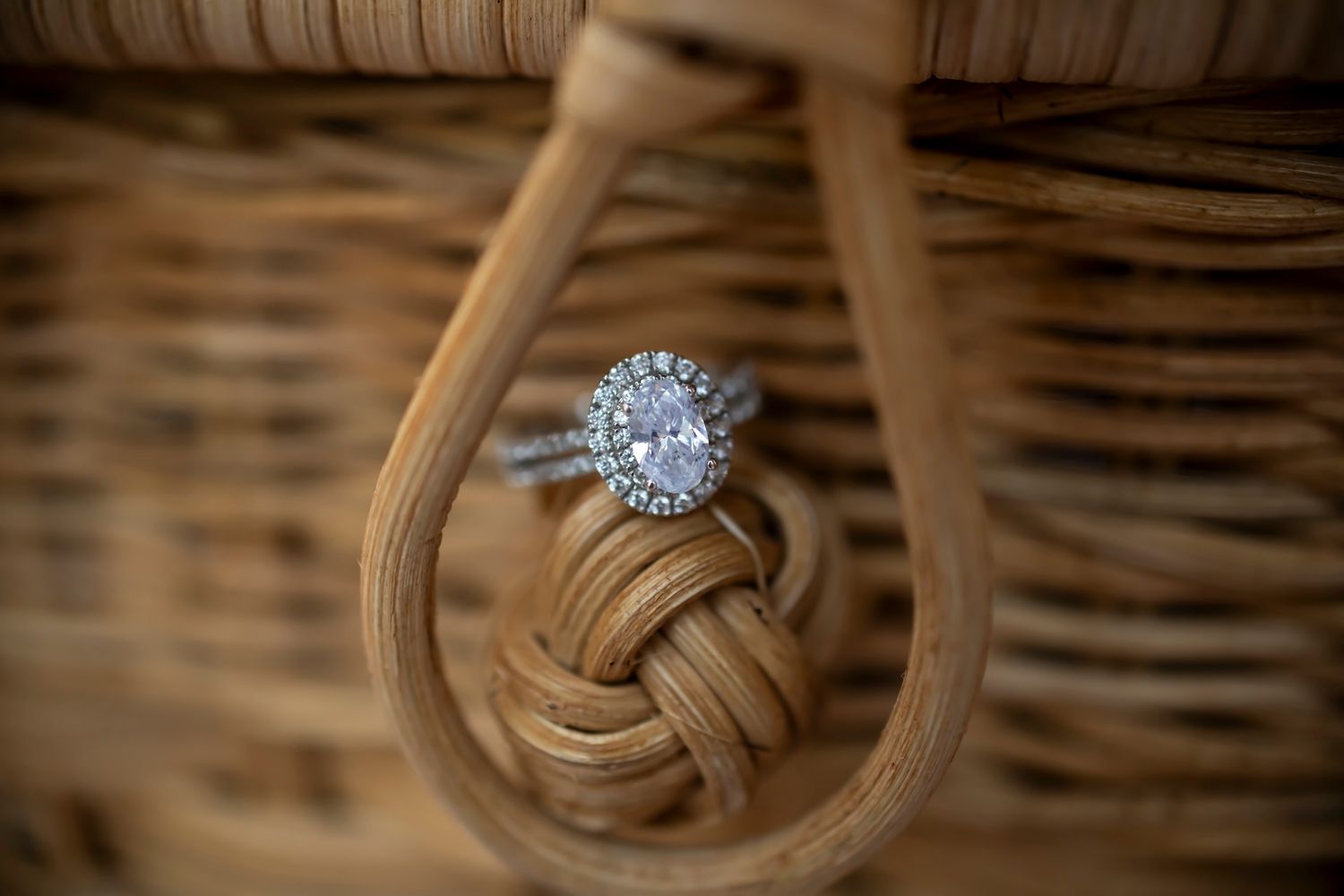 A sparkling diamond engagement ring nestled in a woven leather knot on a rustic wicker backdrop.