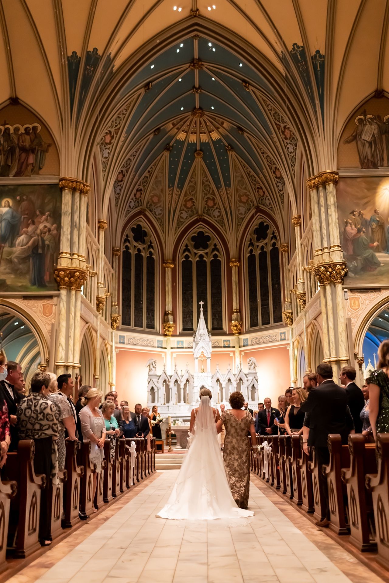 A panoramic view of a grand cathedral wedding ceremony with guests seated in wooden pews beneath Gothic arches.