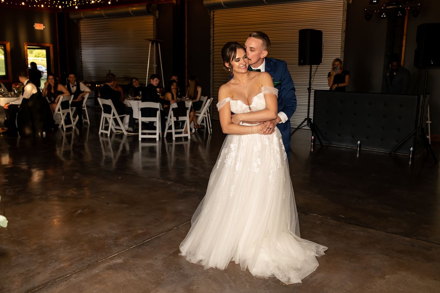 Couple in formal wedding attire dancing together on a dark wooden dance floor at an evening reception.