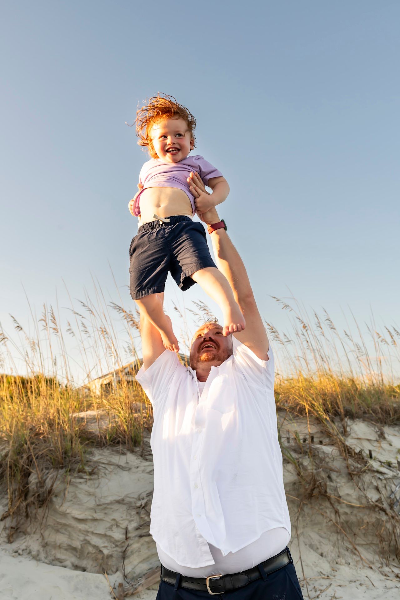 A sequence of four photos shows a small child being playfully lifted into the air against a sand dune backdrop at sunset.