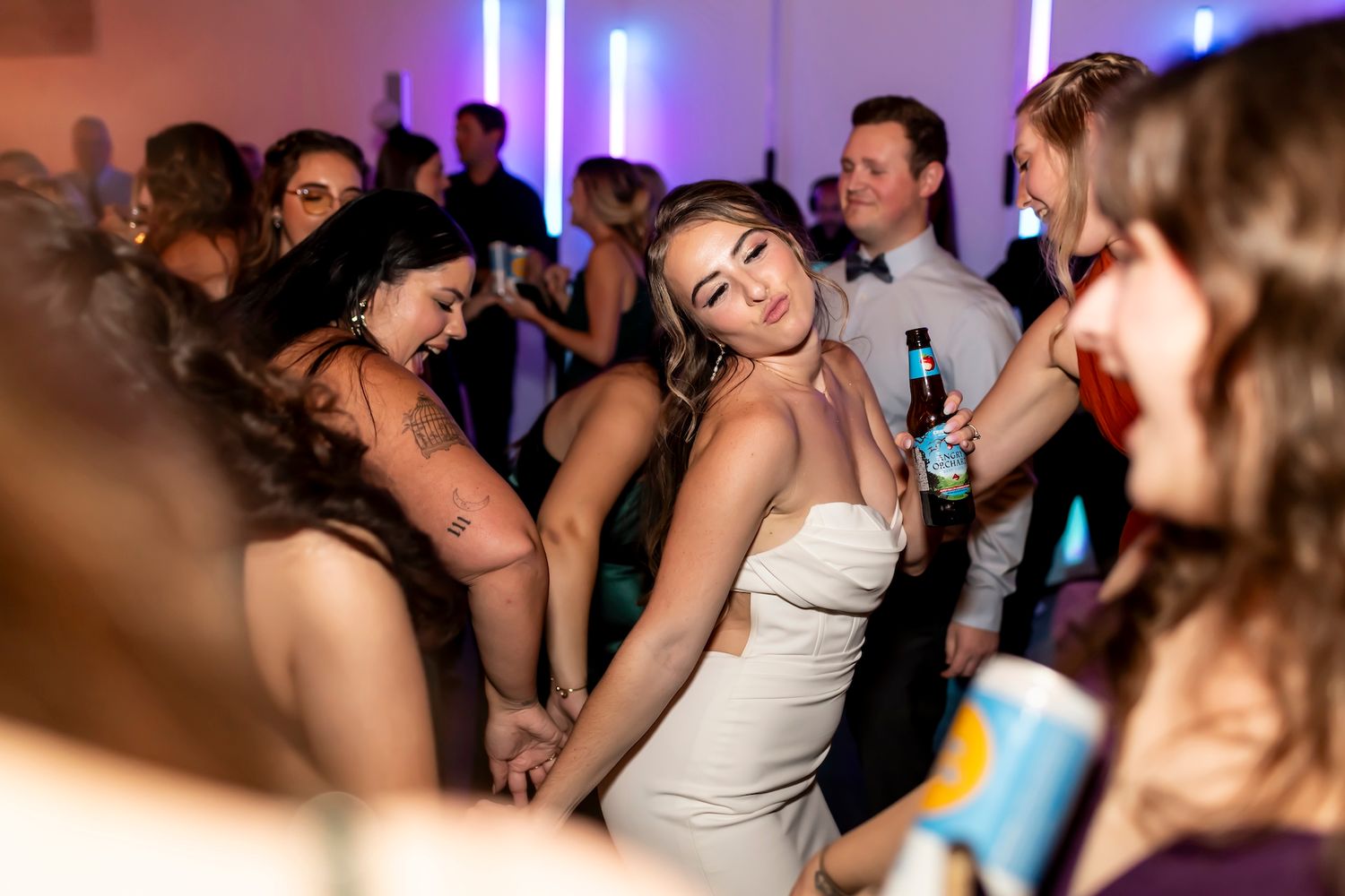 People dancing and having fun at an energetic wedding reception with purple lighting and a festive atmosphere.