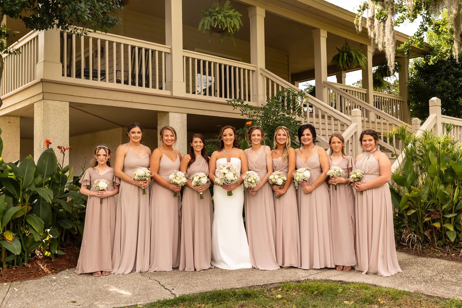 A row of bridesmaids in blush pink dresses stand together on the steps of a classic southern estate.