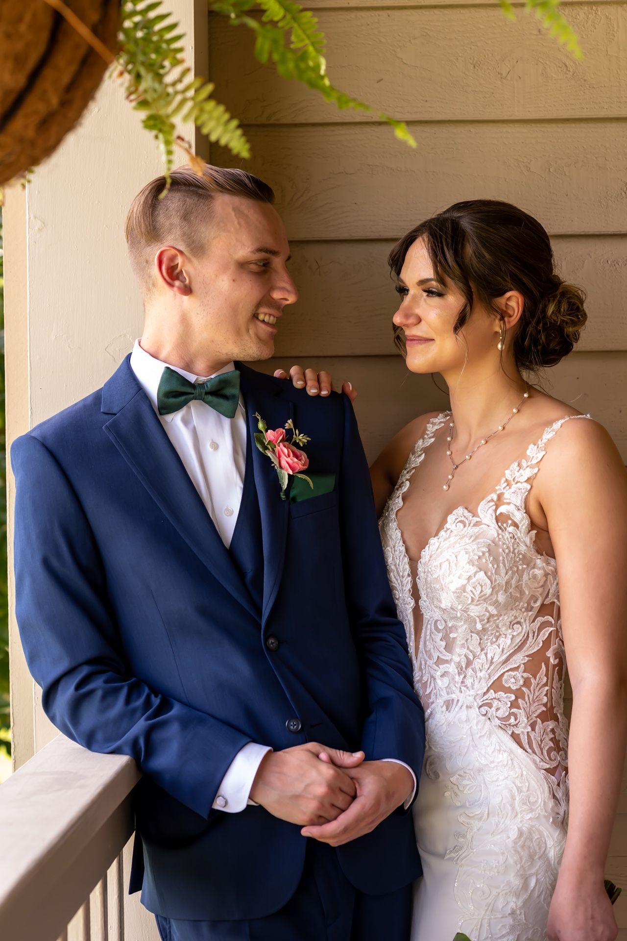 Couple shares an intimate moment on their wedding day, with bride in lace gown and groom in navy suit with bow tie.
