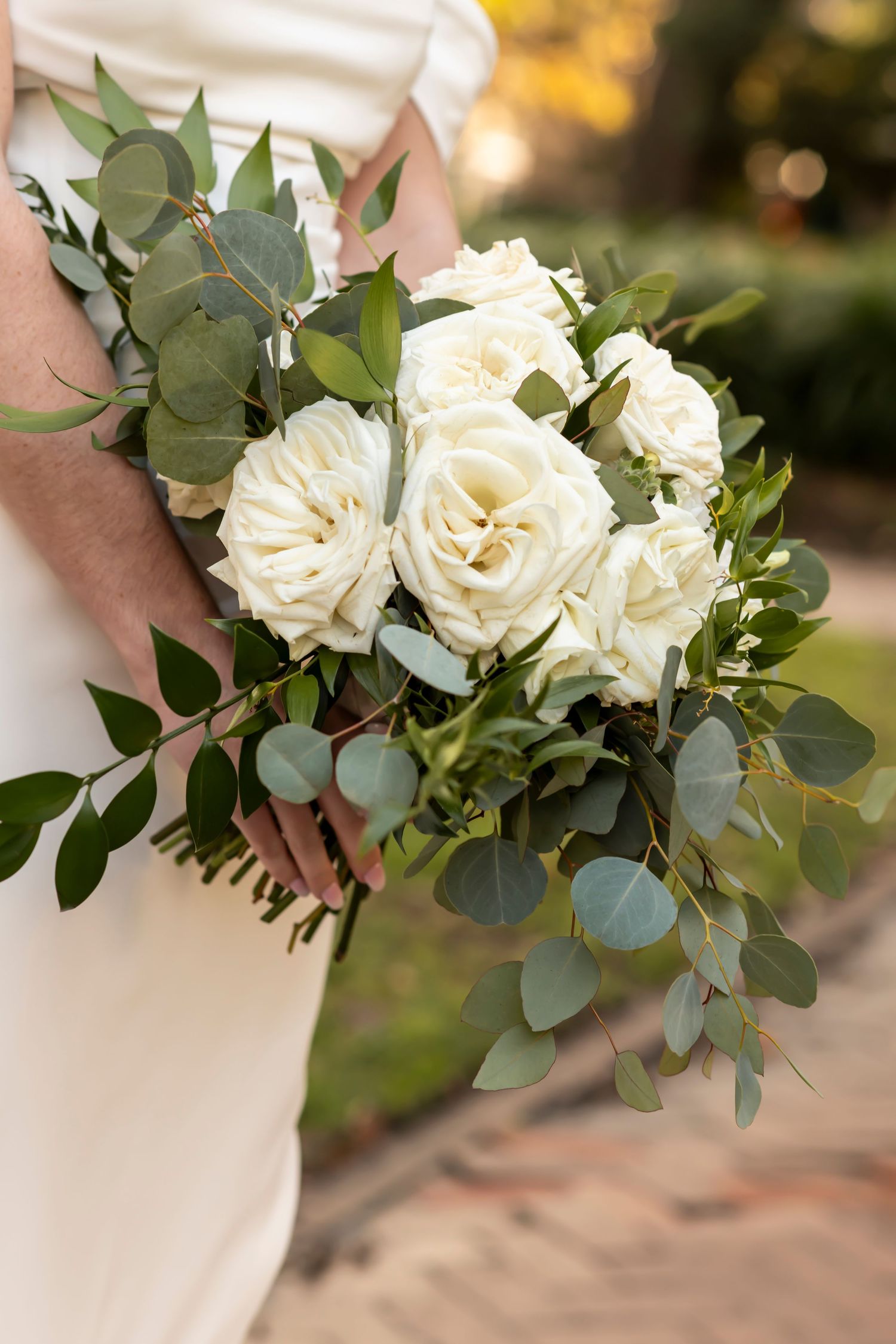 Elegant white rose and eucalyptus wedding bouquet held against a white wedding dress.