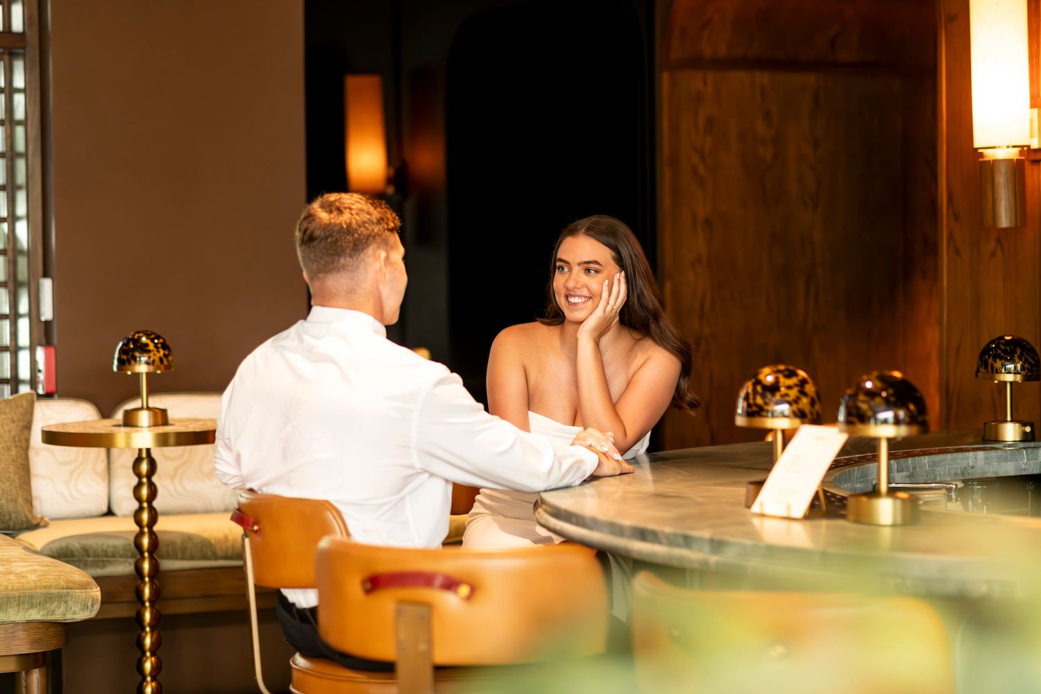 Two people sitting at an illuminated bar counter having an intimate conversation in warm lighting.