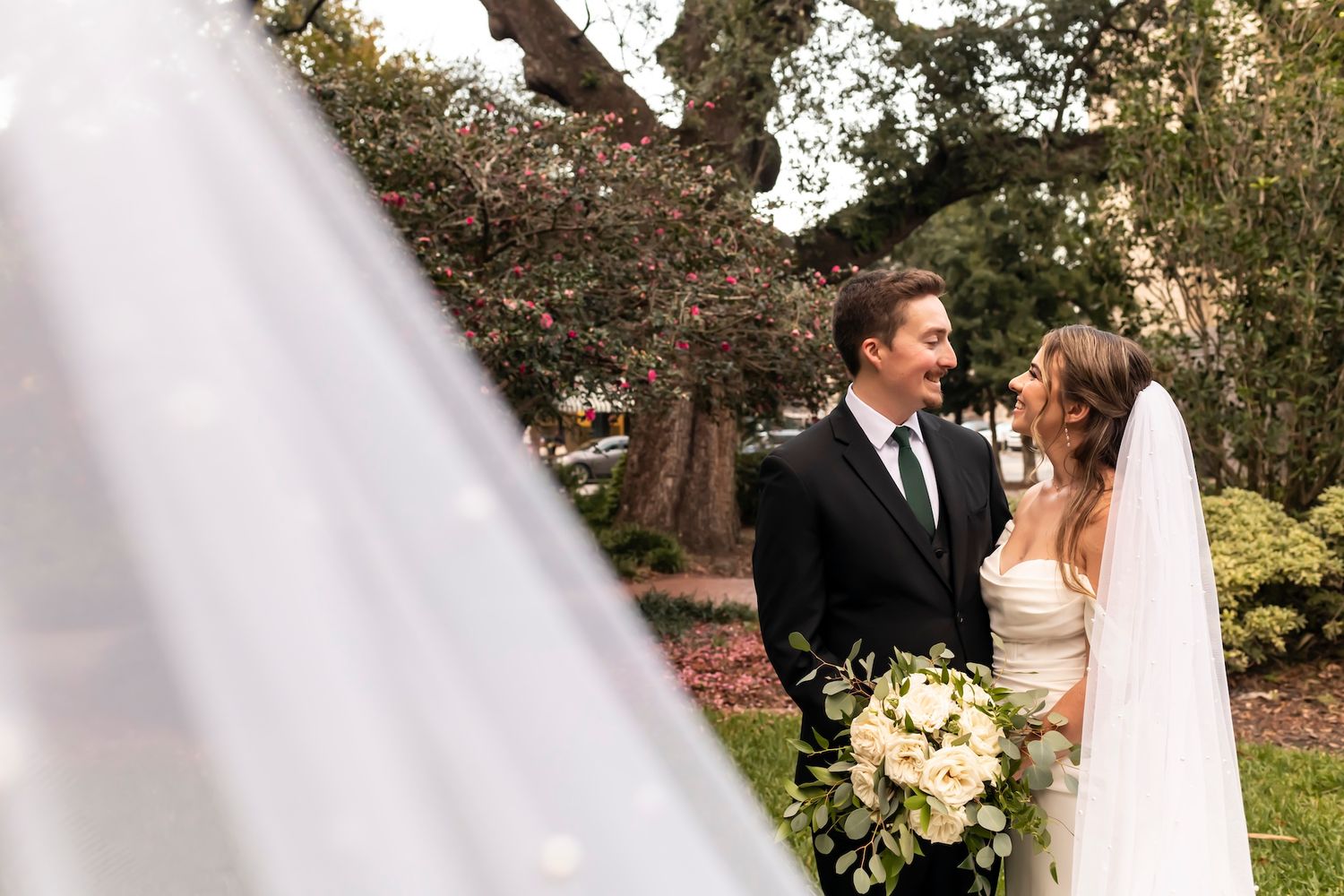 A person in a wedding dress embraces someone outdoors in a sunlit garden setting during a wedding ceremony.