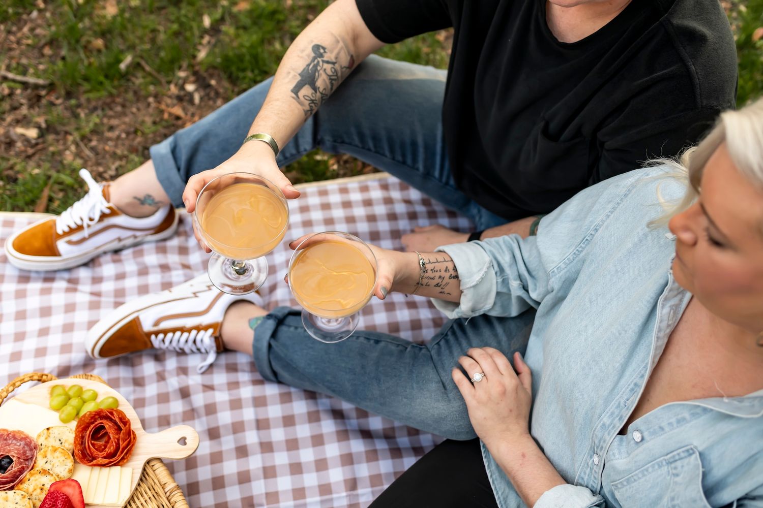 People enjoying a casual outdoor picnic with burgers and snacks on a purple gingham blanket.