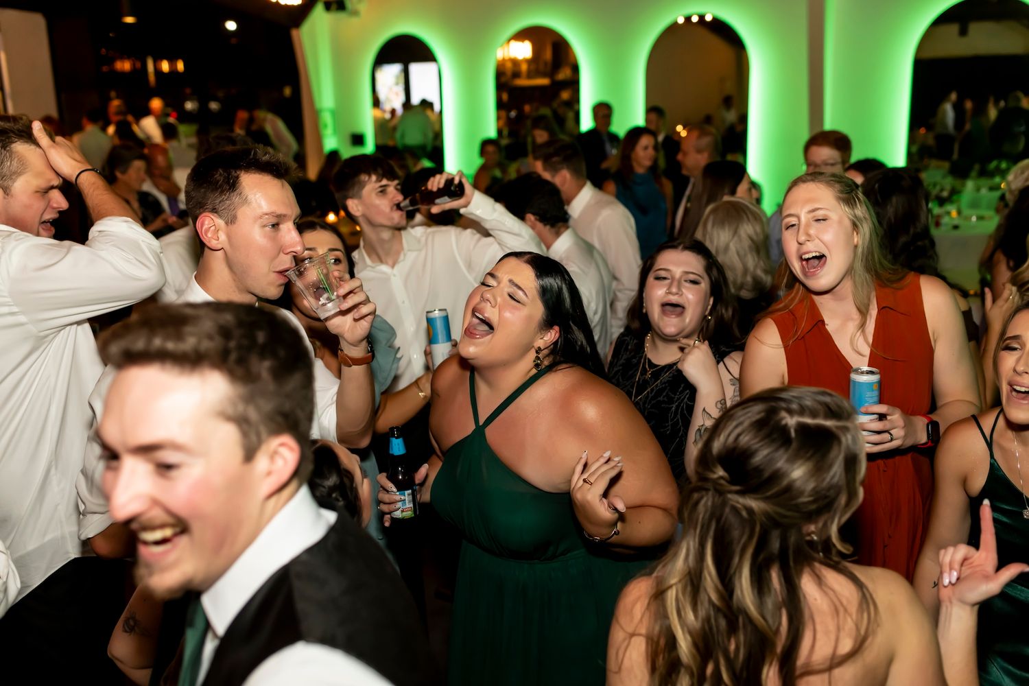 Party guests dancing and celebrating enthusiastically at an event with green uplighting in the background.