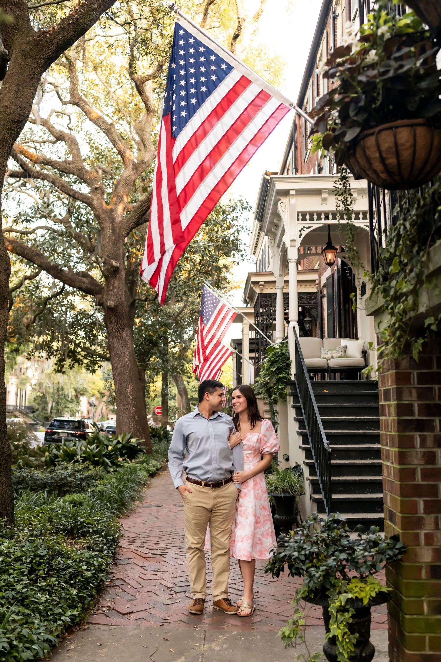 Couple strolls along a charming brick pathway lined with trees and historic buildings as American flags wave in the breeze.