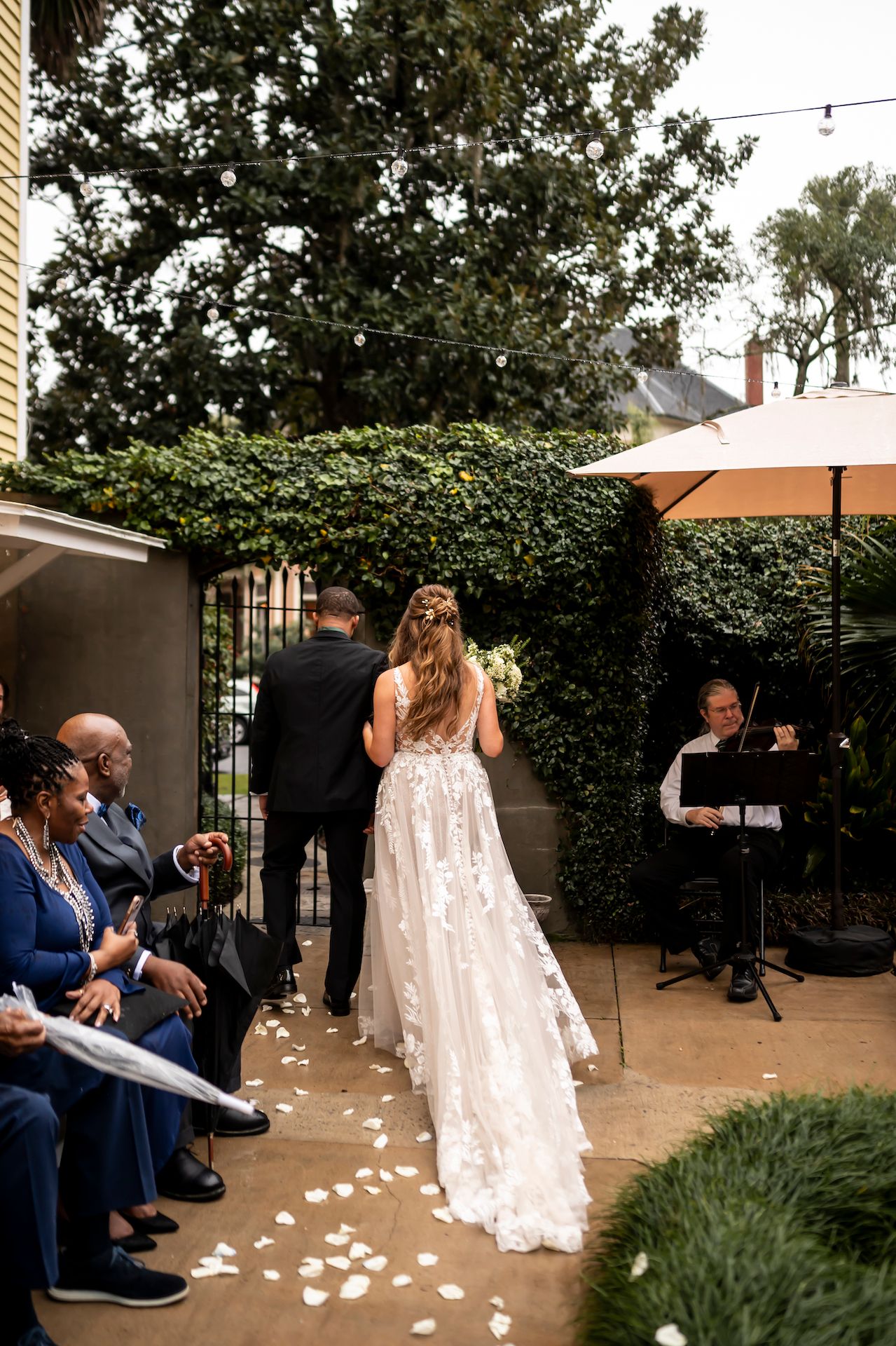 An outdoor wedding ceremony with white flower petals scattered along the walkway under a patio umbrella.