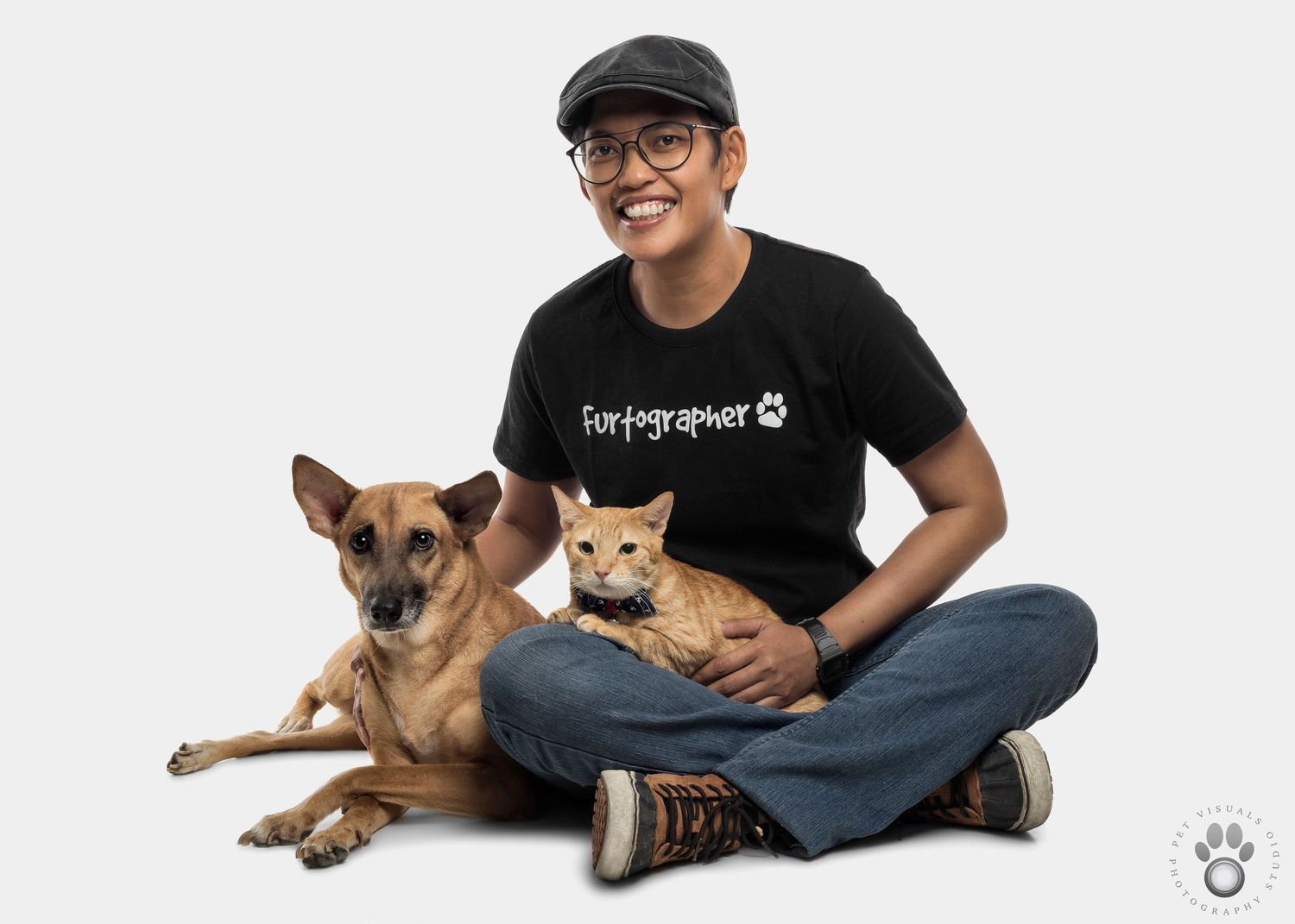 Person in black t-shirt and jeans sits on floor petting a mixed breed dog and orange cat.