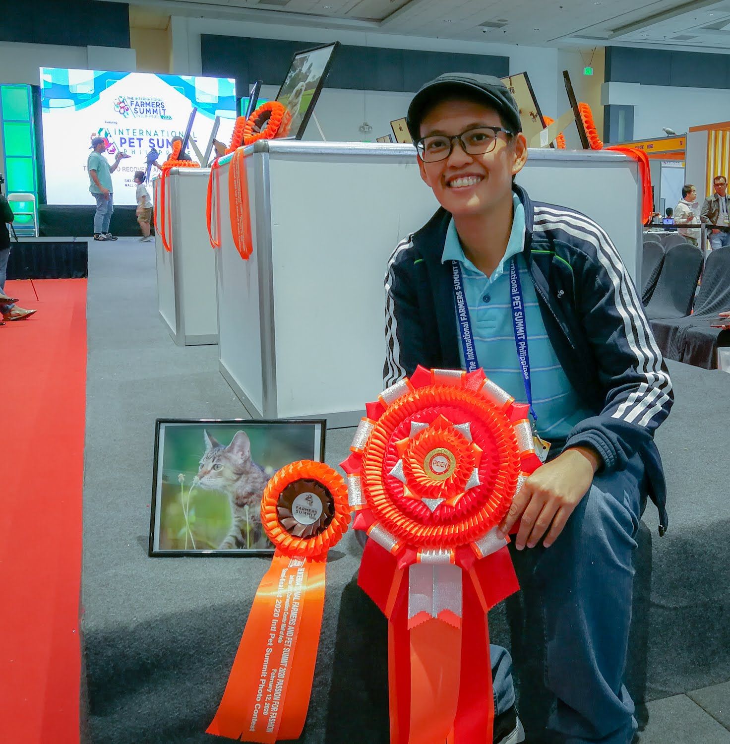 Someone holds a large red and orange achievement ribbon with multiple rosettes at what appears to be a conference or event.