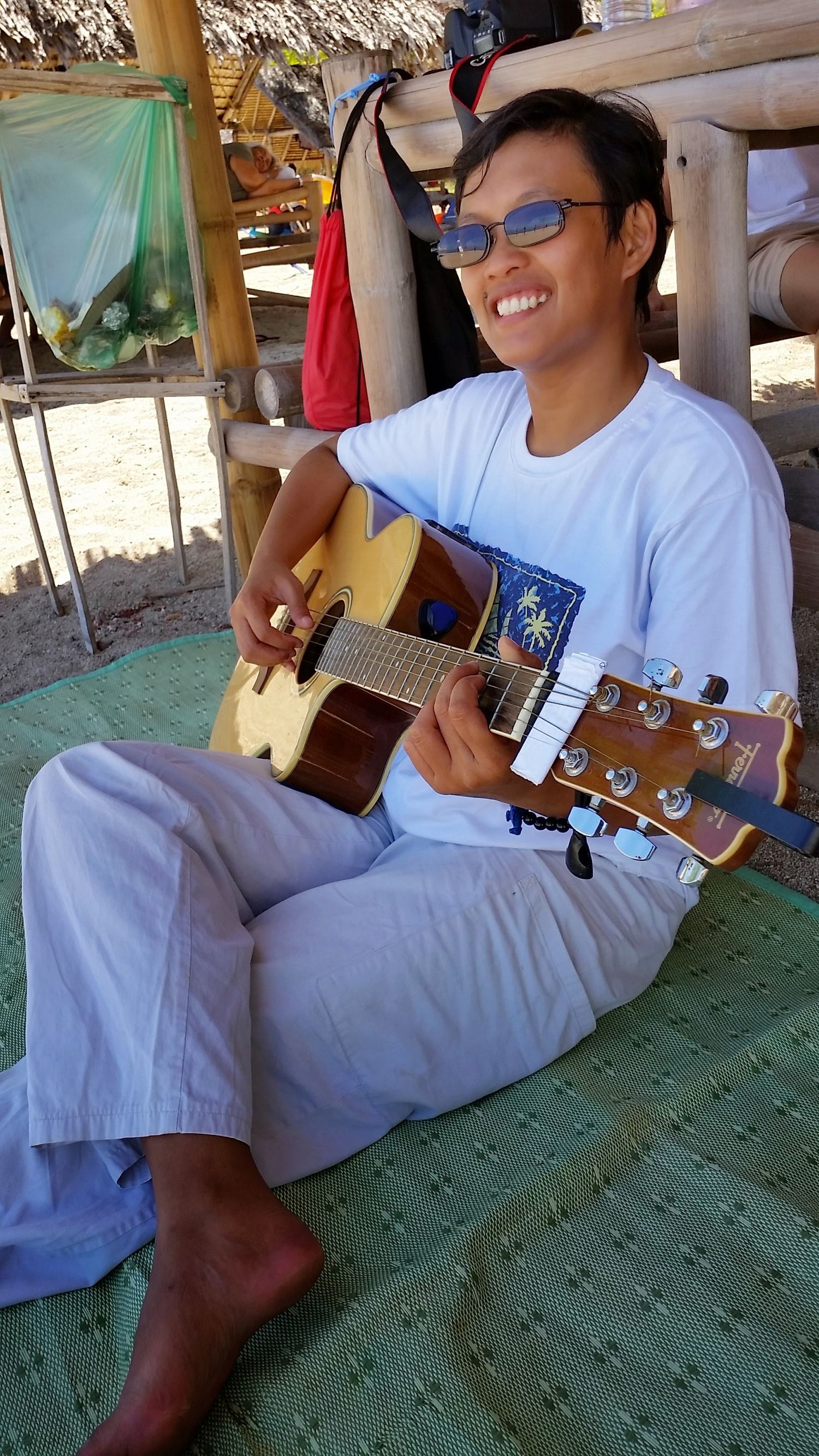 Four sequential photos show someone in white clothing playing an acoustic guitar while relaxed on a textured floor mat.