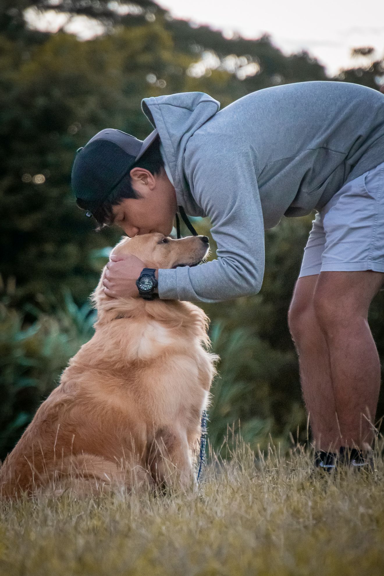a man kissing her golden retriever at the park