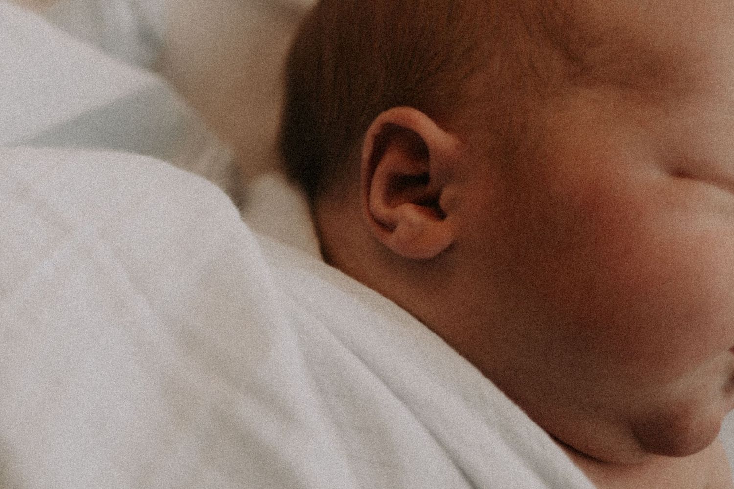 Close-up detail of sleeping newborn's ear and cheek against white blanket.