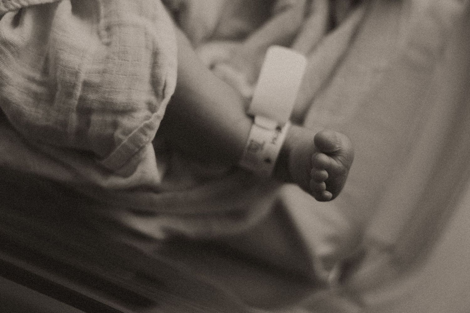 Close-up profile view of sleeping newborn swaddled in white cloth against neutral background.