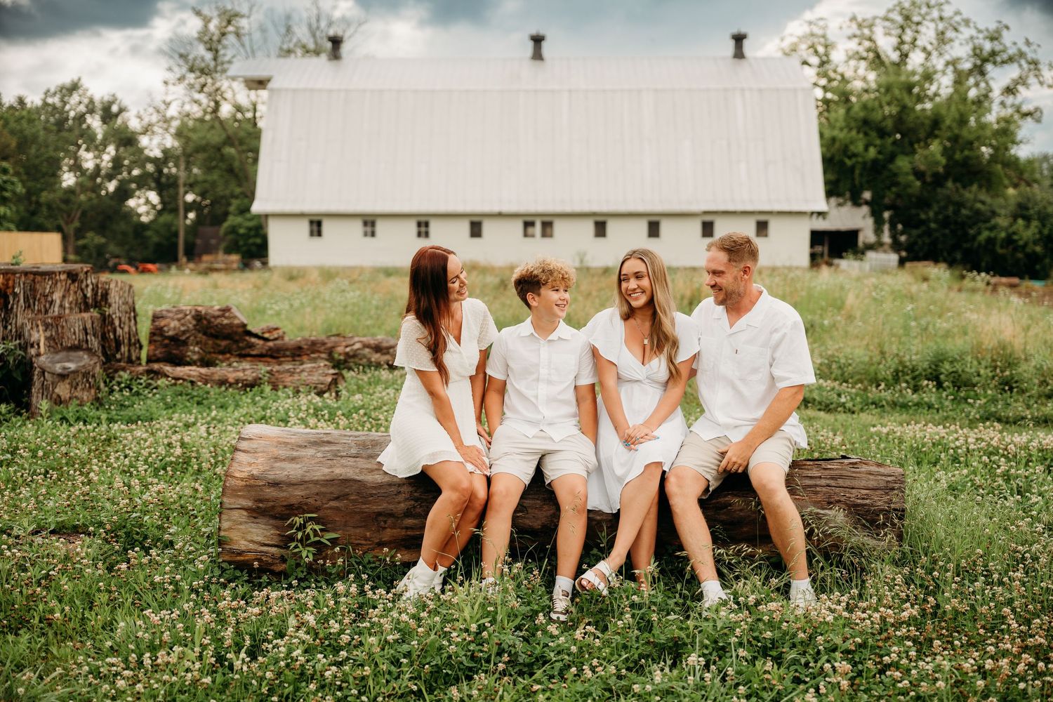 Family wearing white outfits sits together on wooden surfaces in outdoor photo shoot settings under natural lighting.