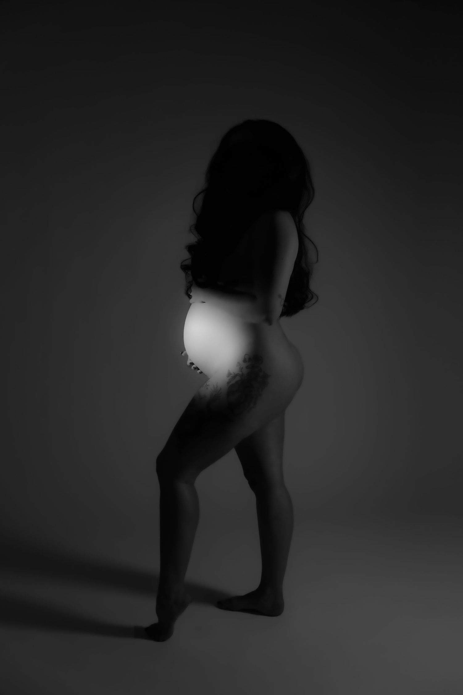 Dramatic silhouette maternity photo against dark background.