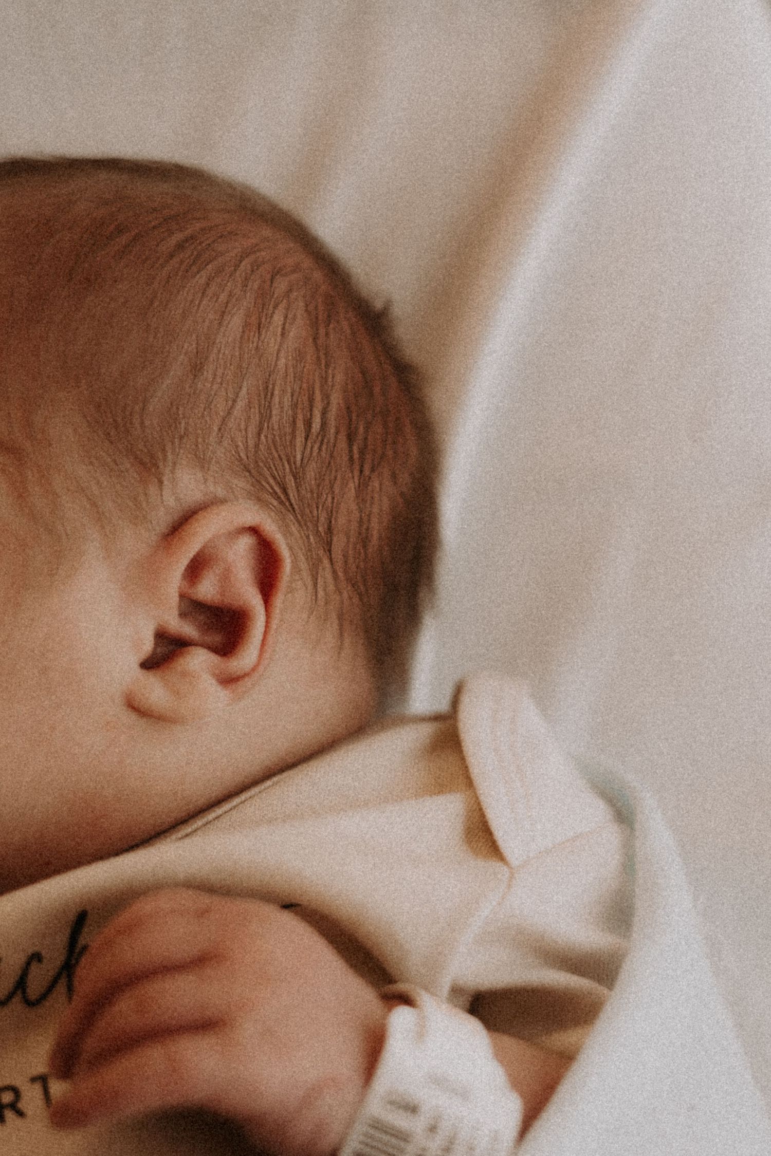Side view of newborn resting against white fabric in muted natural lighting.