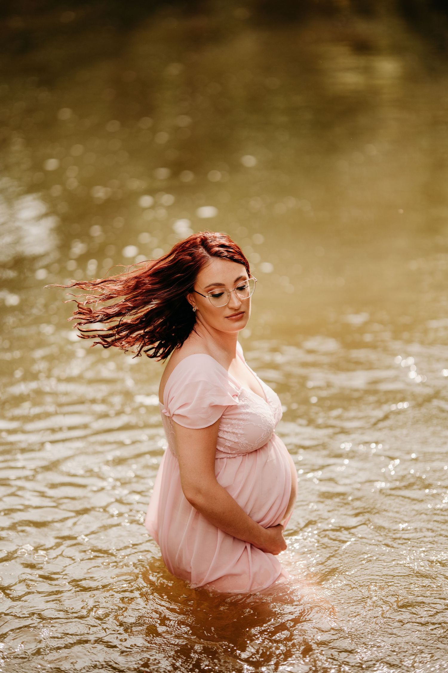 Ethereal water maternity portrait with flowing hair in golden sunlight.
