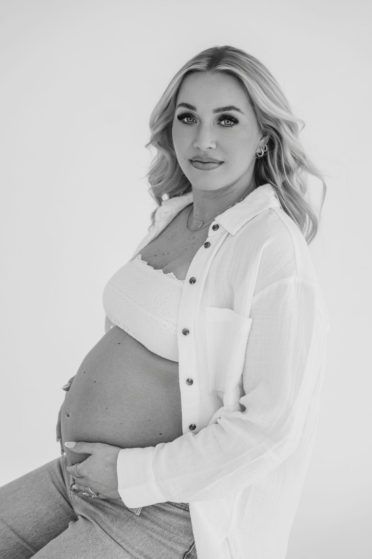 Black and white maternity photo with woman in white button-down against light background.