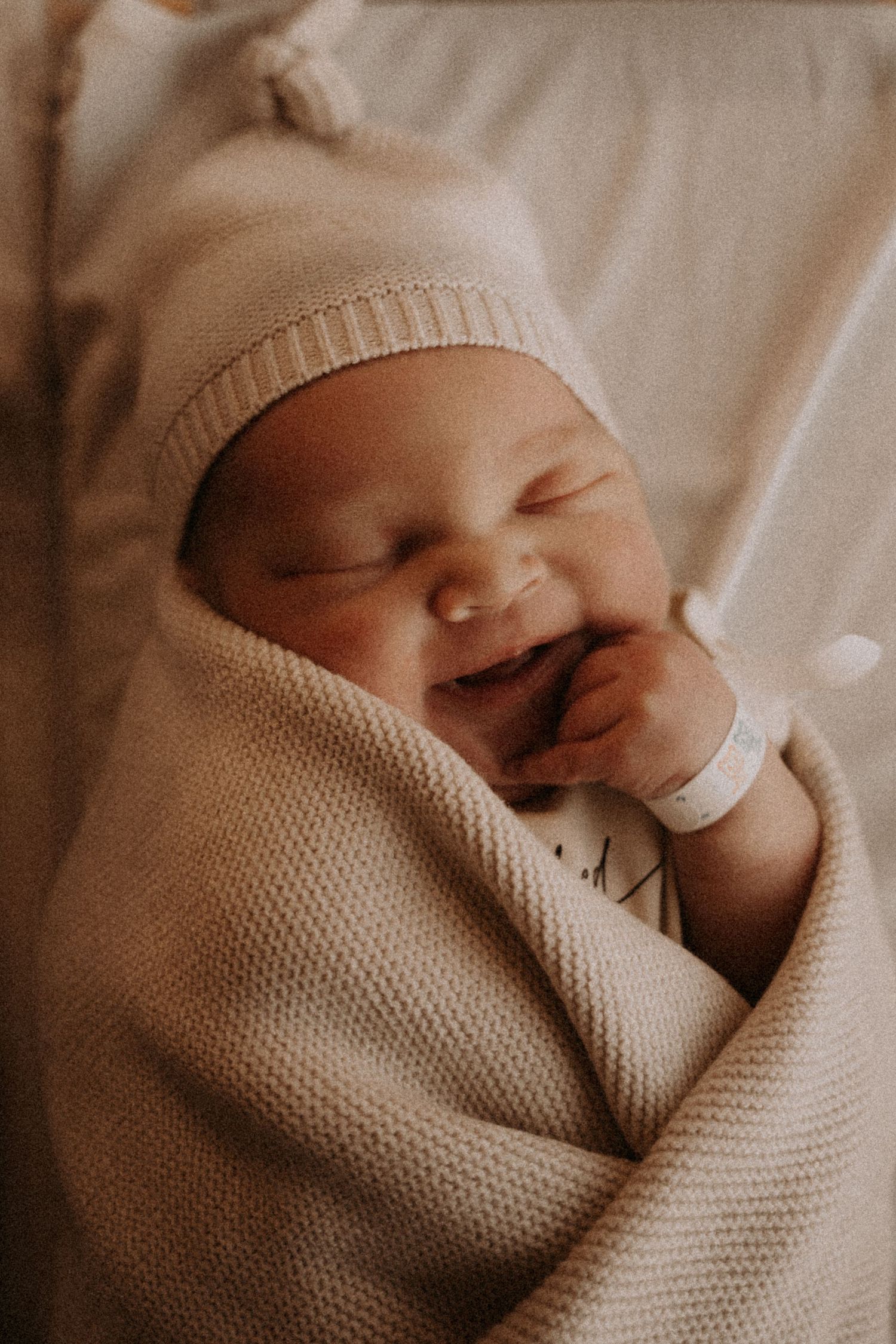 Sweet newborn baby wrapped in soft beige blanket smiling while sleeping.