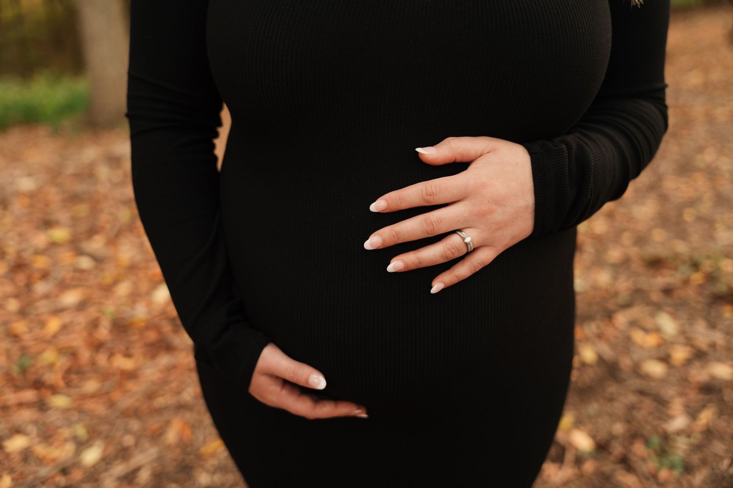 Close-up of hands gently cradling a baby bump in a black maternity dress.