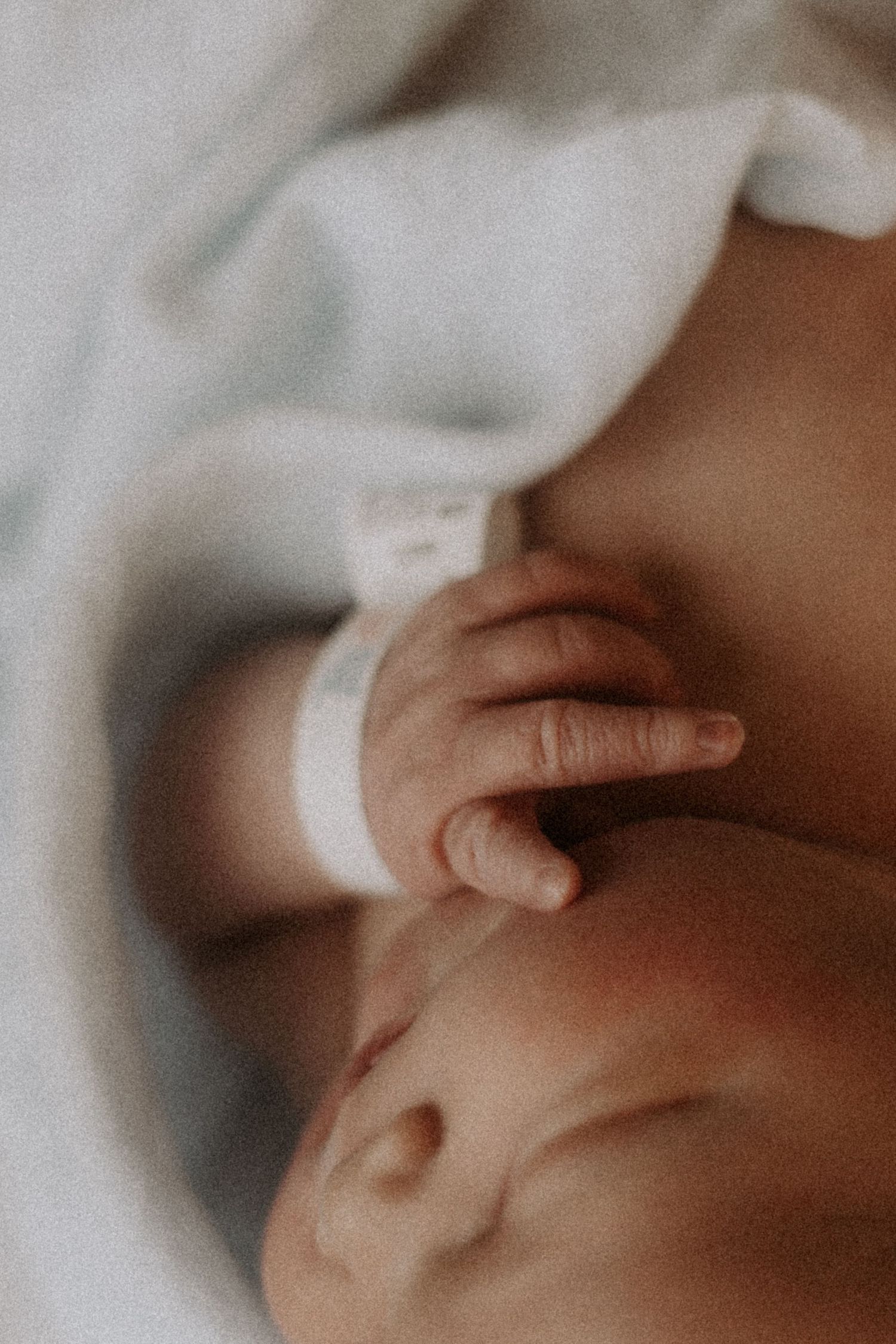 A close-up shot of a newborn baby's tiny hand wearing a hospital bracelet while wrapped in soft white fabric.