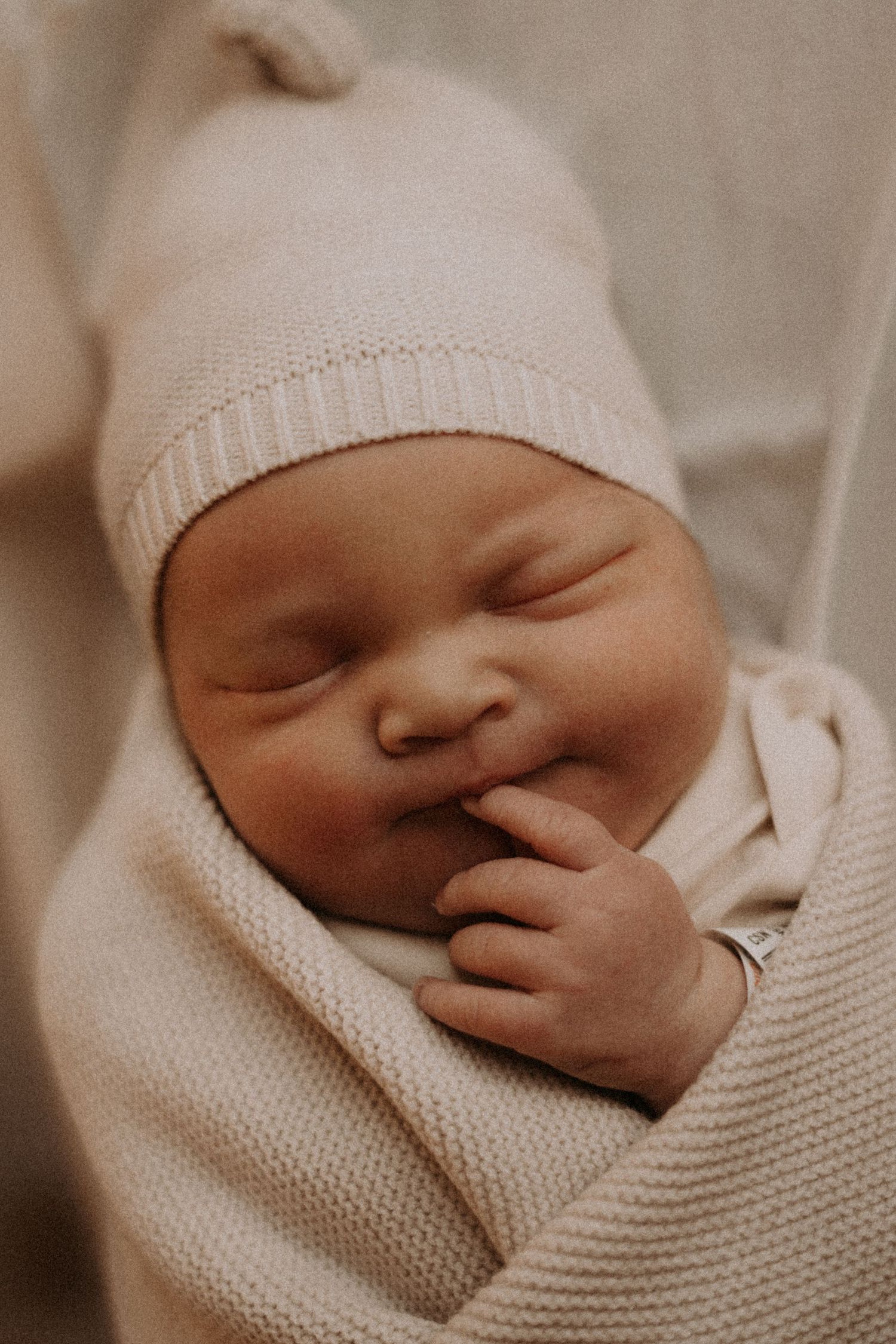 Newborn wearing knit cap peacefully sleeping in soft white blanket.