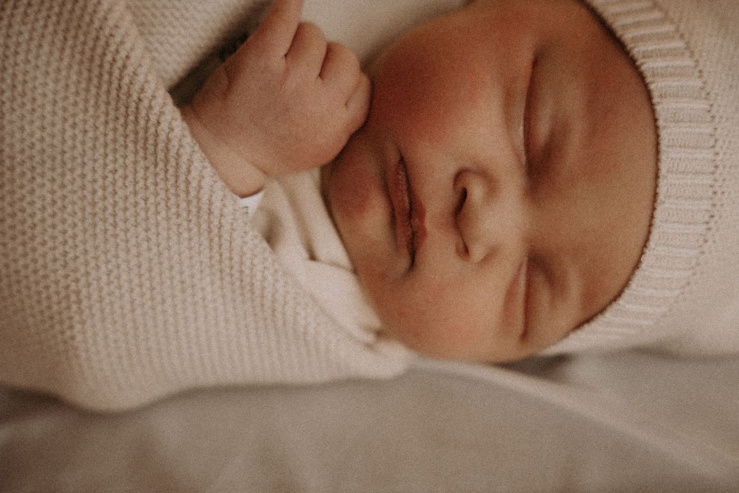 Close-up of sleeping newborn in white knit blanket and hat.