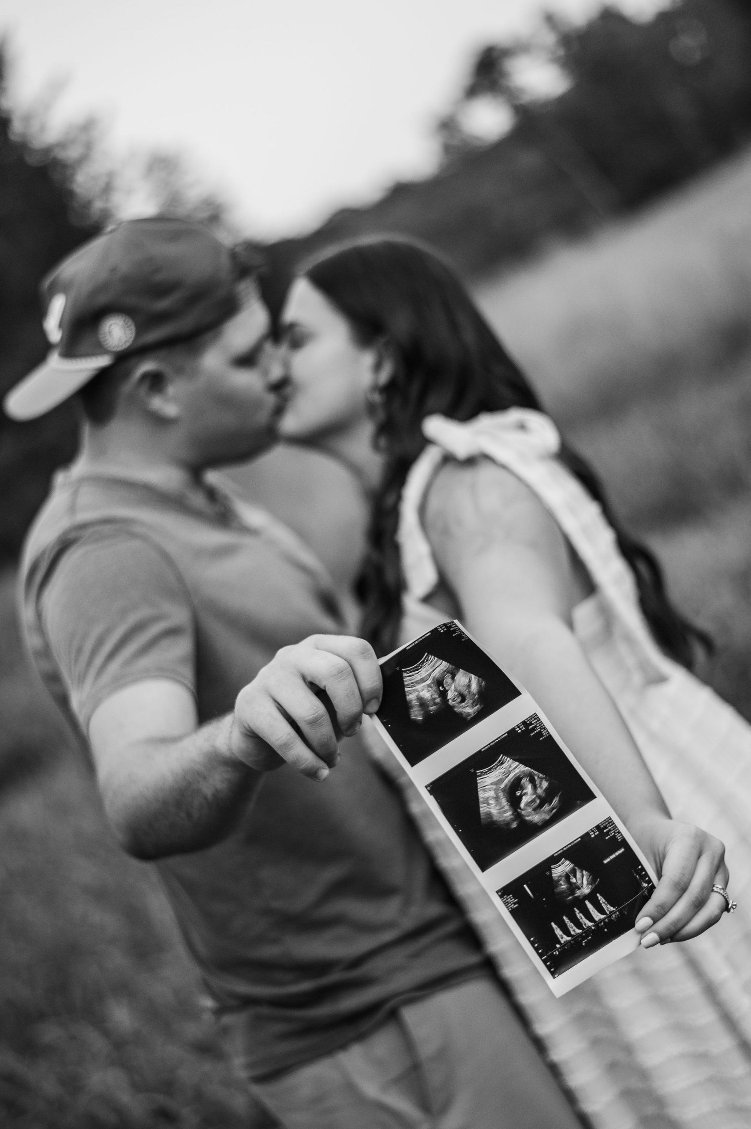 Black and white photo of couple sharing ultrasound photos outdoors.
