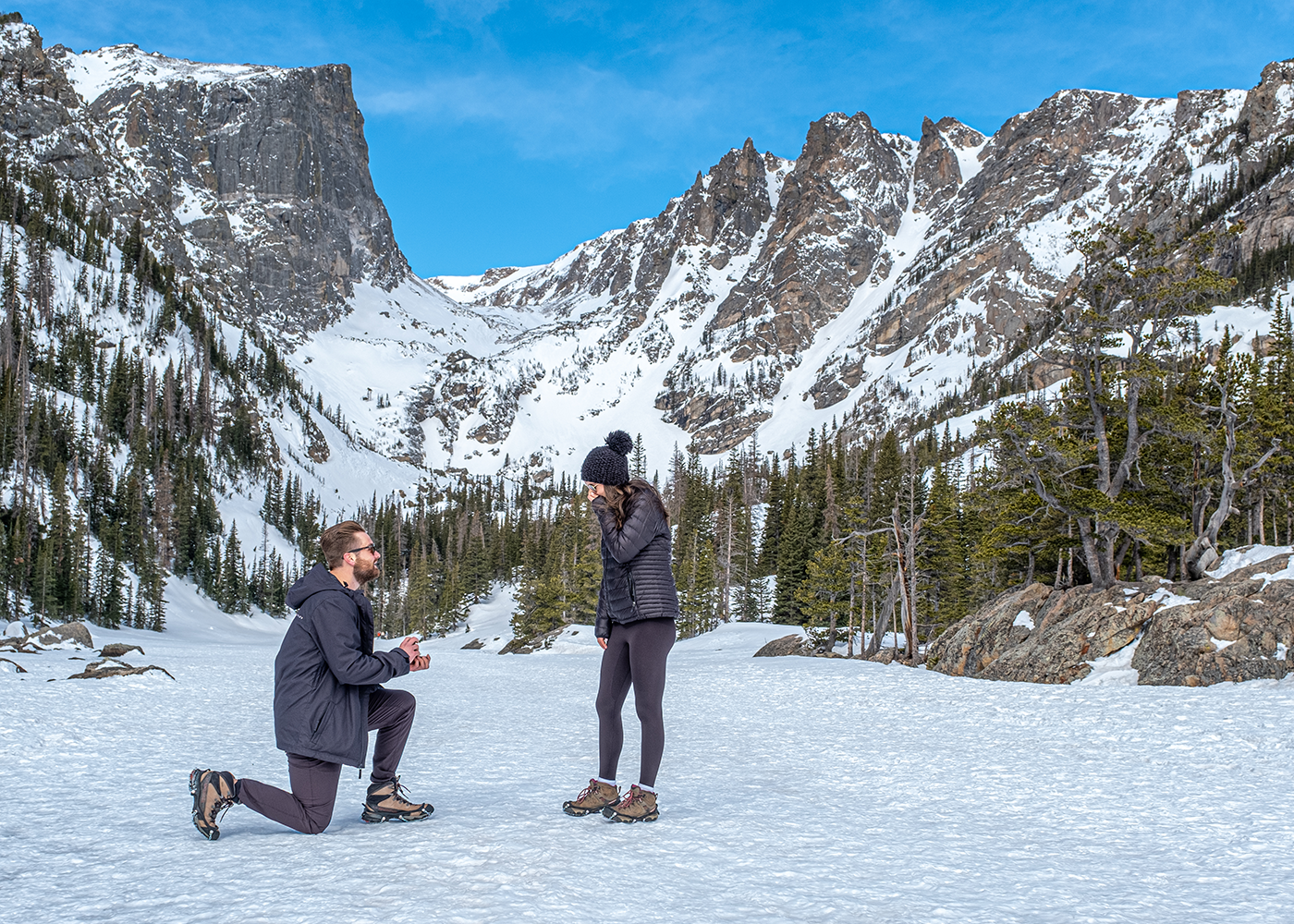 A marriage proposal unfolds against a snowy mountain backdrop in Rocky Mountain National Park at Dream Lake