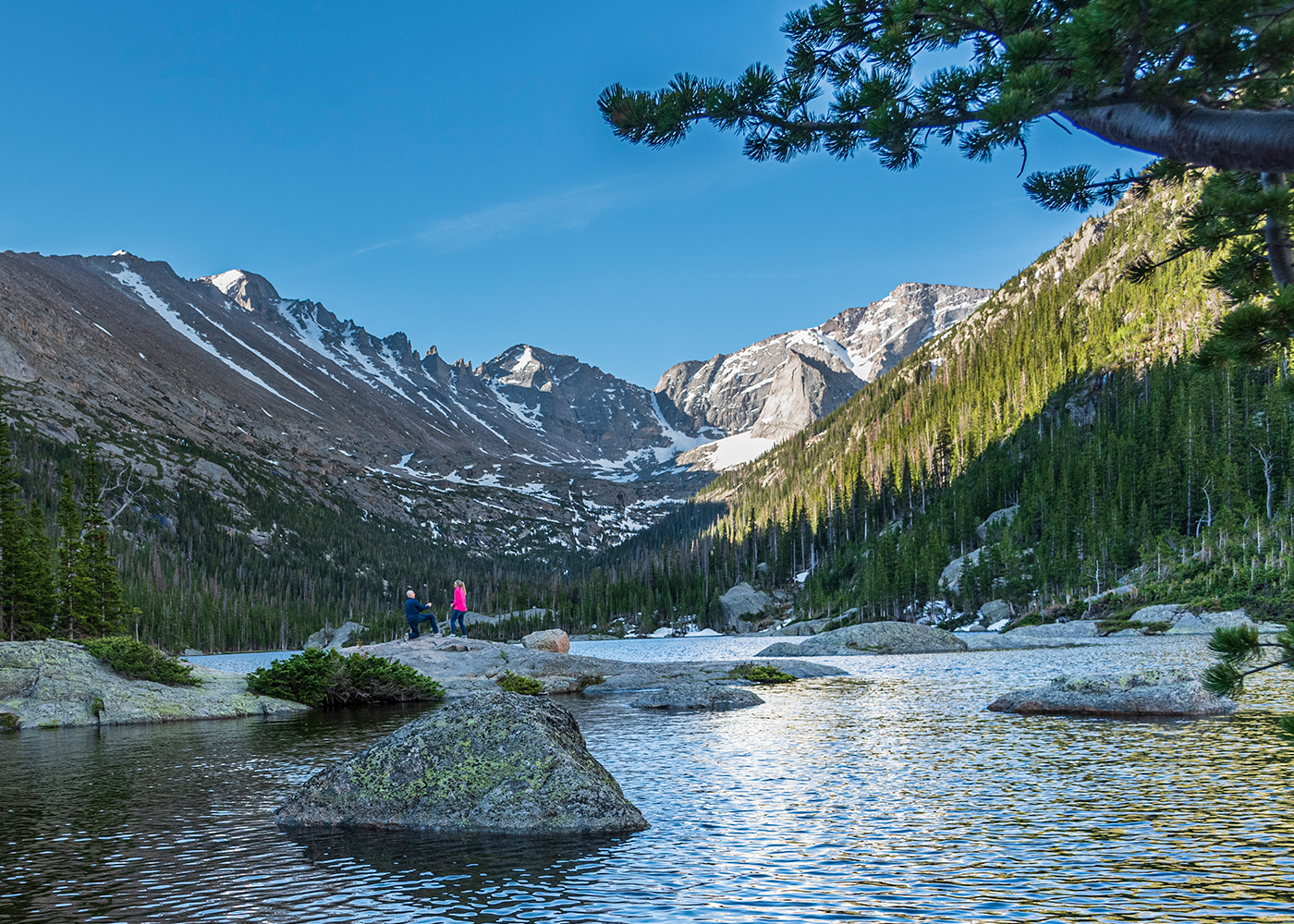 Snow-capped mountain peaks reflect in a serene alpine lake in a panoramic wilderness marriage proposal at Mills Lake in RMNP