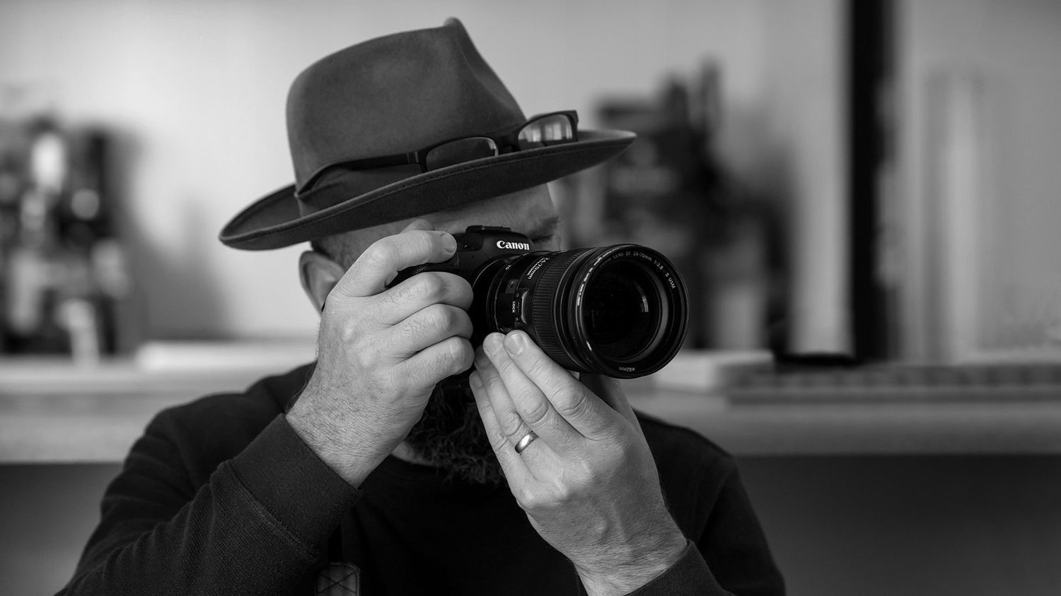 A black and white Image of Jason Robins wearing his Akubra Hat, a Professional photographer taking a photo with a Canon DSLR camera.