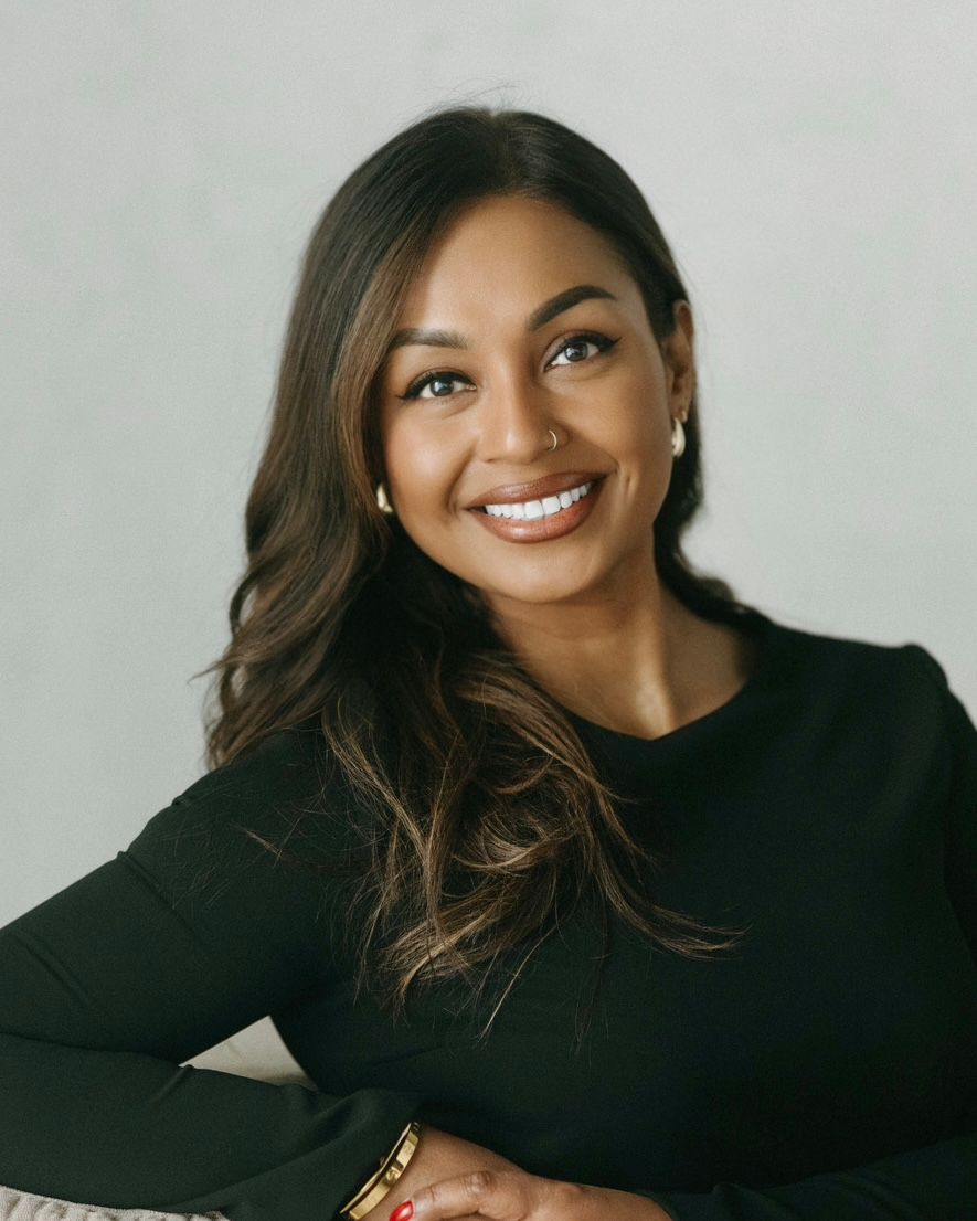 Professional headshot of someone wearing a black long sleeve top and smiling warmly against a light gray background.
