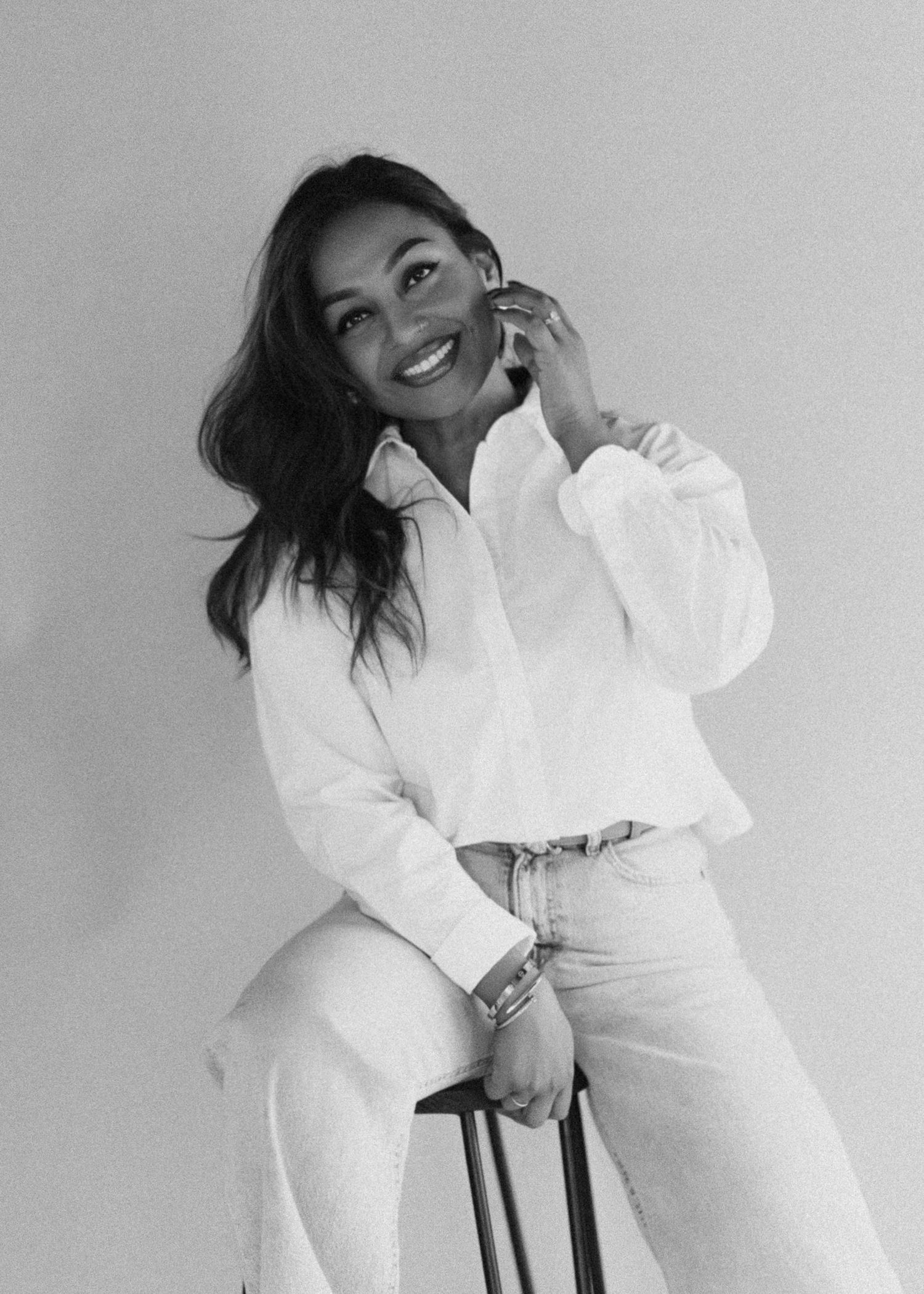 Black and white portrait of someone in a casual chic outfit with white button-down shirt and light pants against neutral background.
