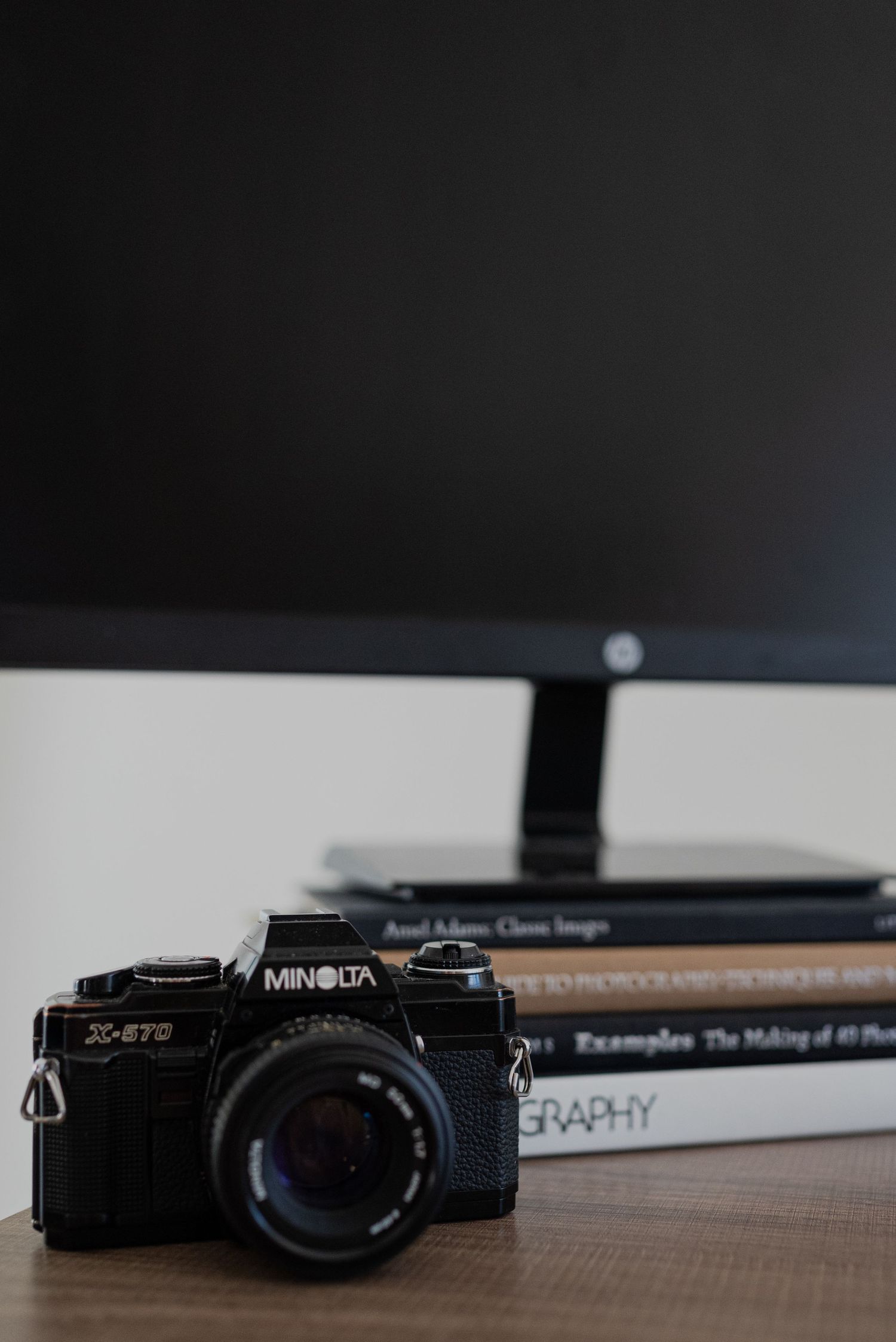 A vintage Minolta camera displayed next to photography books on a wooden desk.