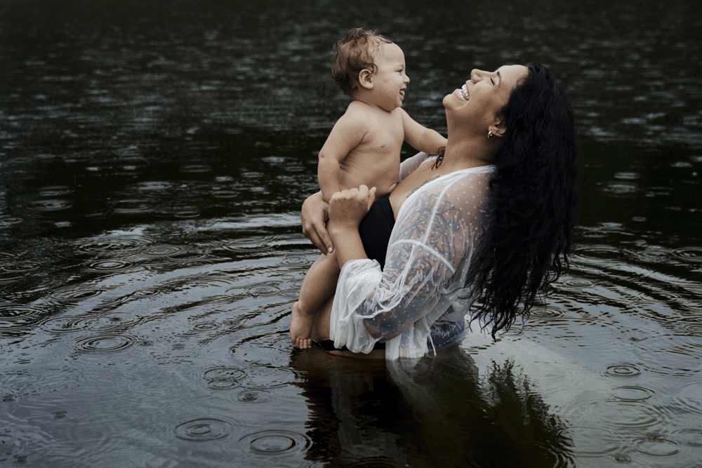 A tender moment between mother and baby playing together in a lake while wearing white flowy clothing.