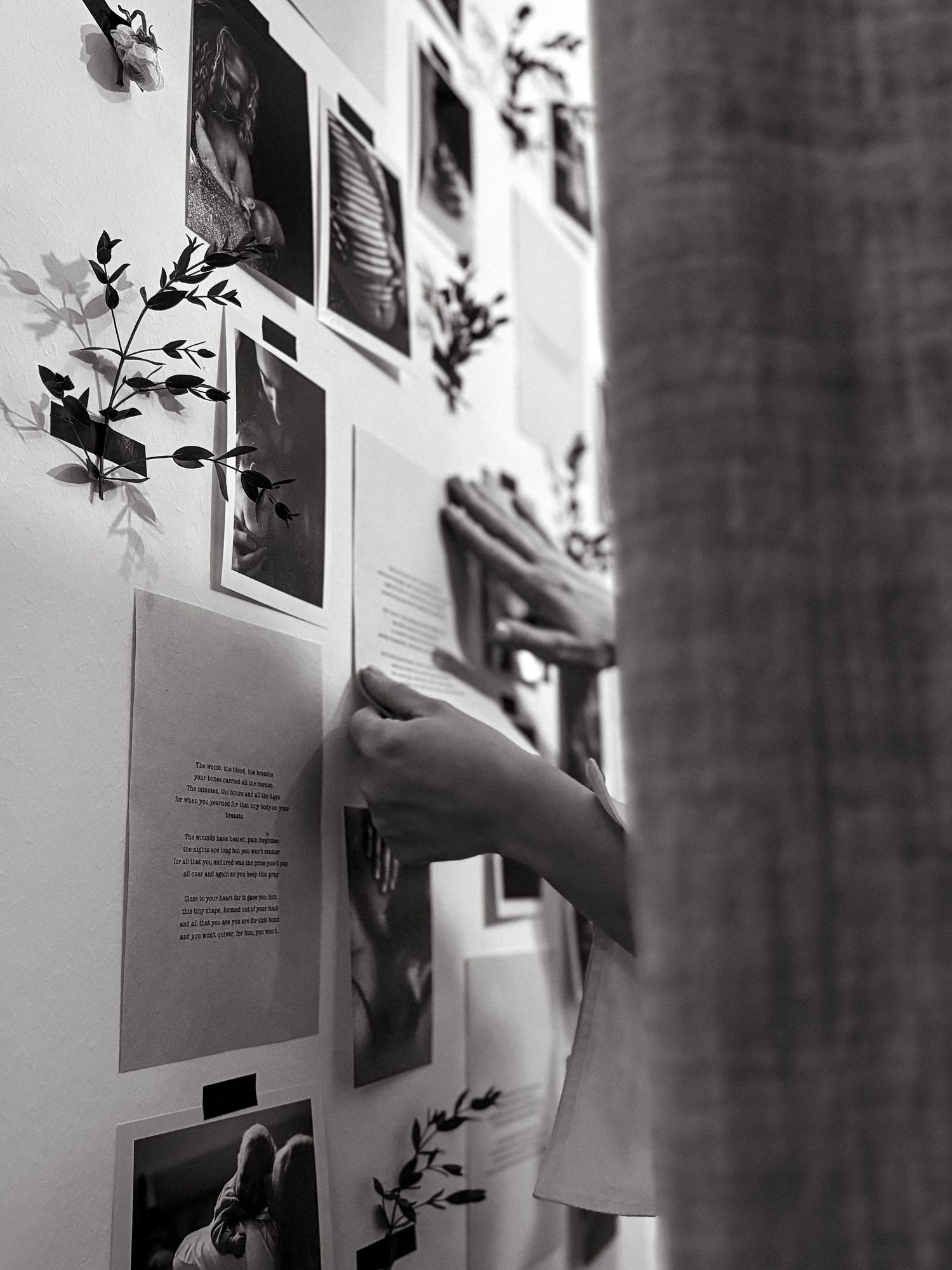 detail of hands attaching a sheet of paper with poem to a photo wall during exhibition for motherhood photographer in Stockholm