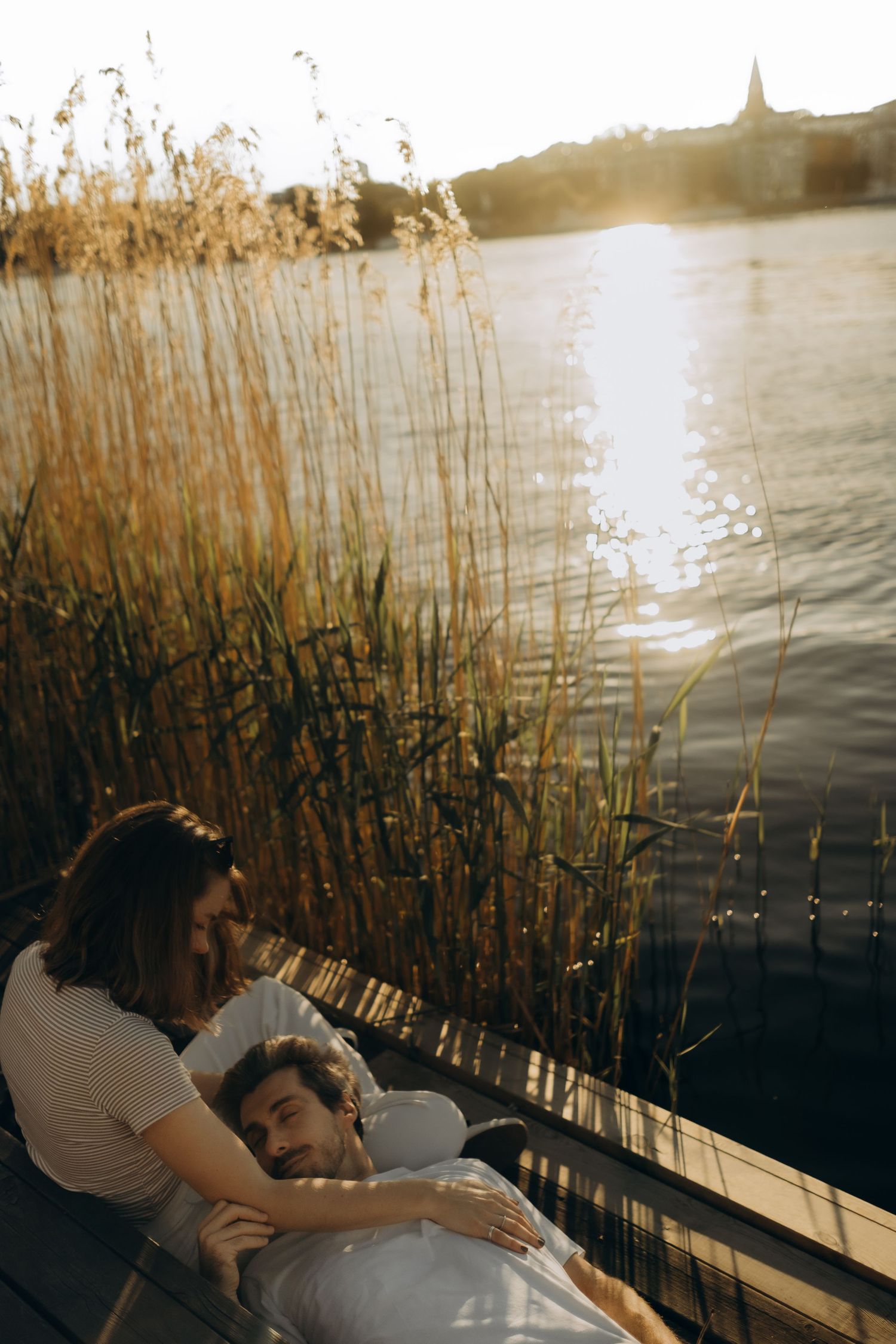 man lying in his girlfriend's lap near water during sunset while being captured by documentary cinematic couple photographer in Stockholm