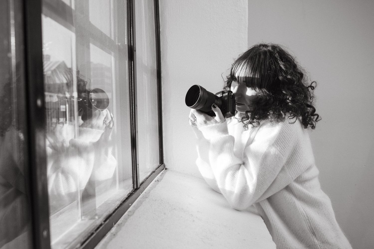 family photographer in Stockholm holding her camera to her face looking out of the window in a studio