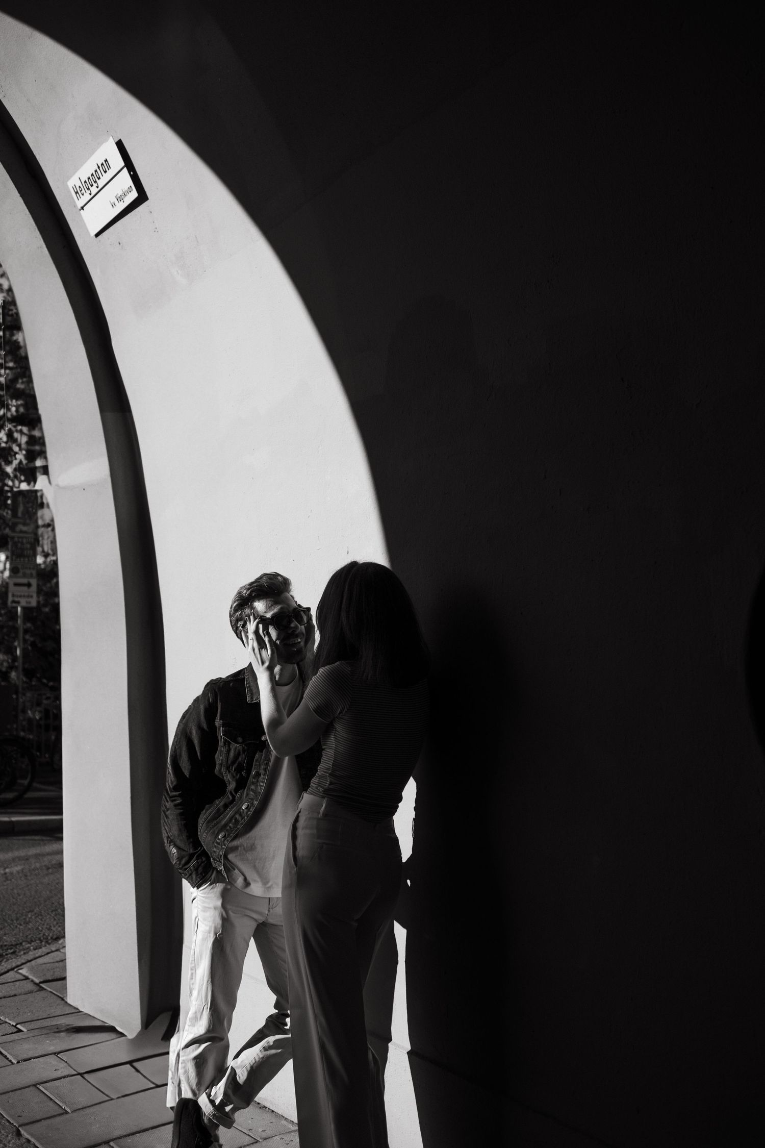 couple looking at each other standing in a shadow near a wall in Stockholm while being captured by a Stockholm couple photographer