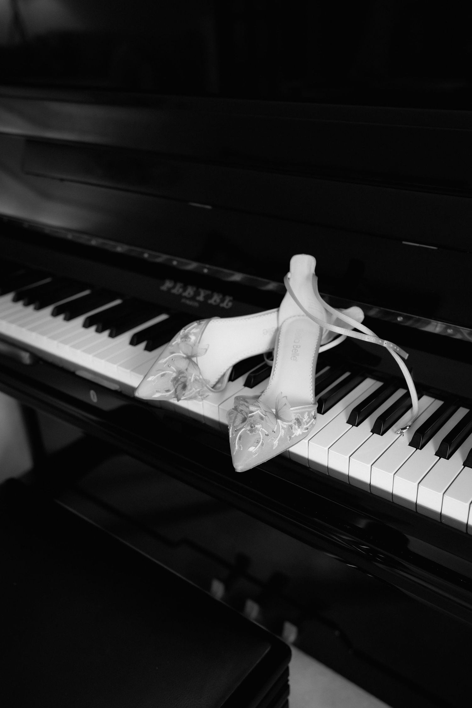 A pair of white ballet pointe shoes rests gracefully on black and white piano keys in dramatic lighting.