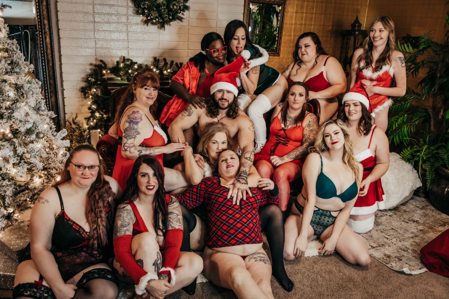 A festive holiday gathering of people wearing red and green outfits posing together by a decorated Christmas tree.