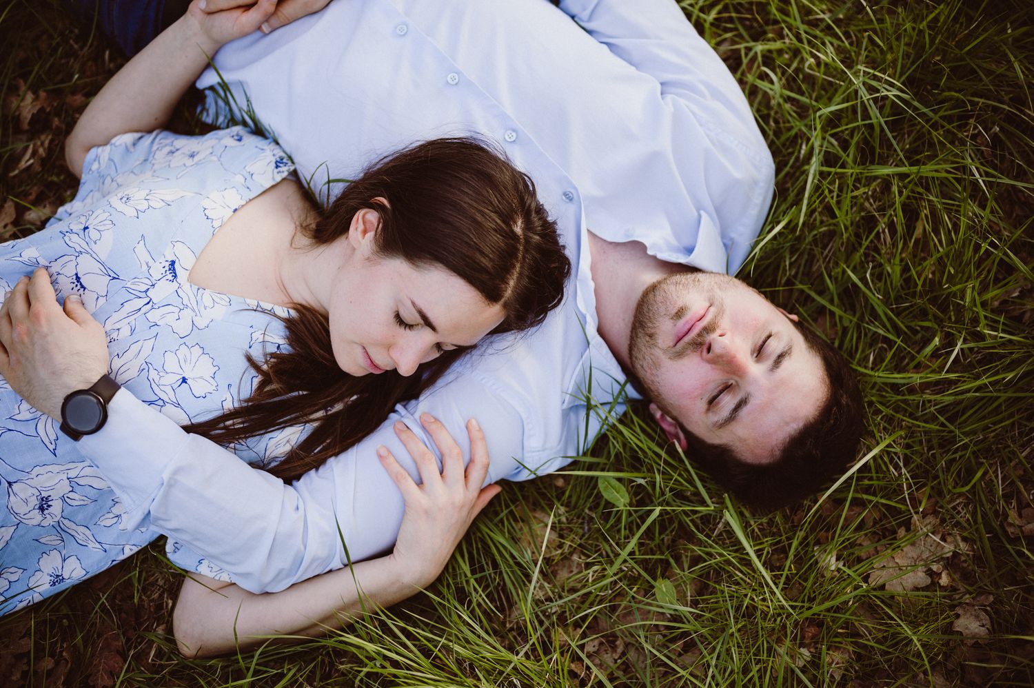 Two people lying on grass wearing light blue and white clothing viewed from above in an artistic portrait.