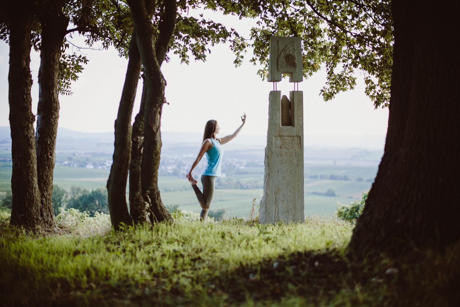Silhouette of person jumping playfully between trees near stone monument at sunset.