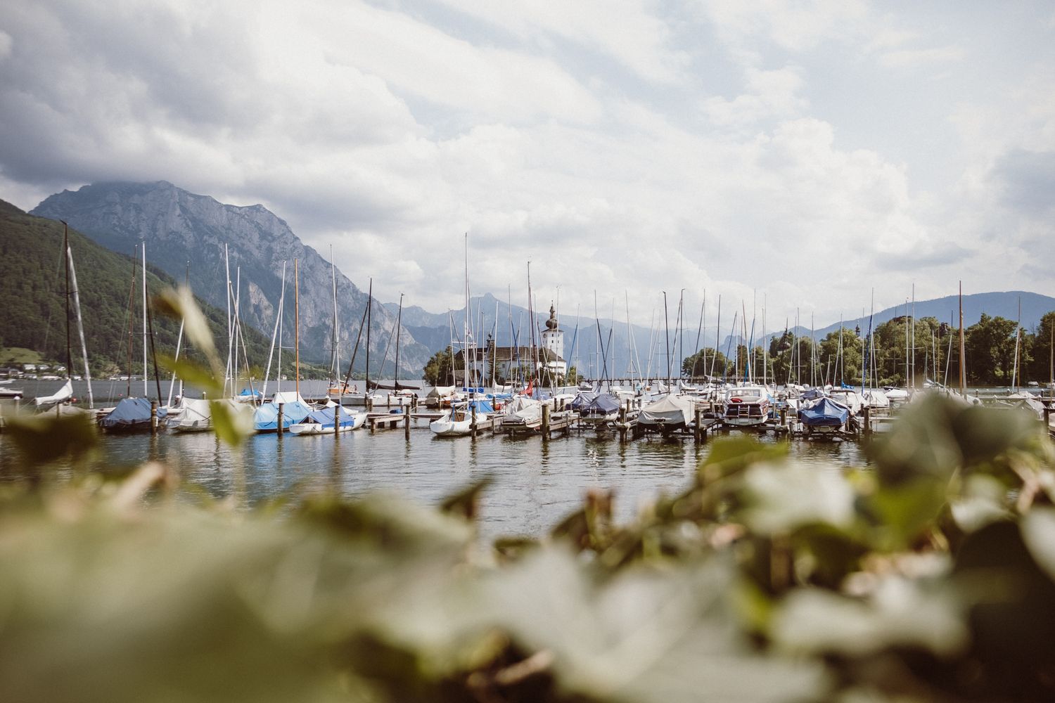 Scenic mountain landscape with marina and boats docked in calm waters on an overcast day.