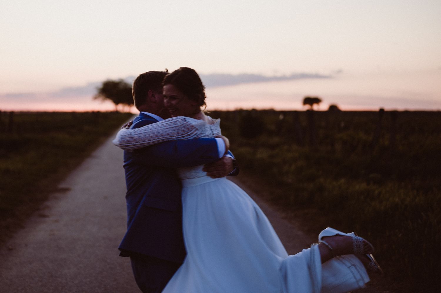 Two people embrace on a path at sunset with dark silhouettes against the glowing sky in the background.