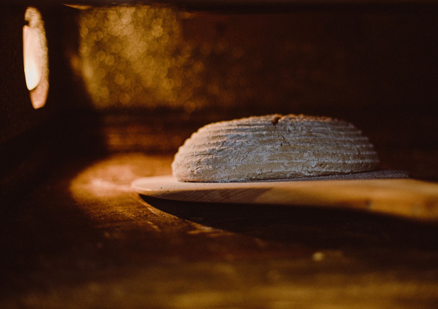Fresh bread loaf baking in rustic wood-fired oven with warm ambient lighting.